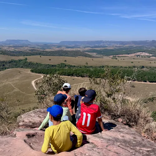 Crianças sentadas numa pedra observando a vista da serra do alto